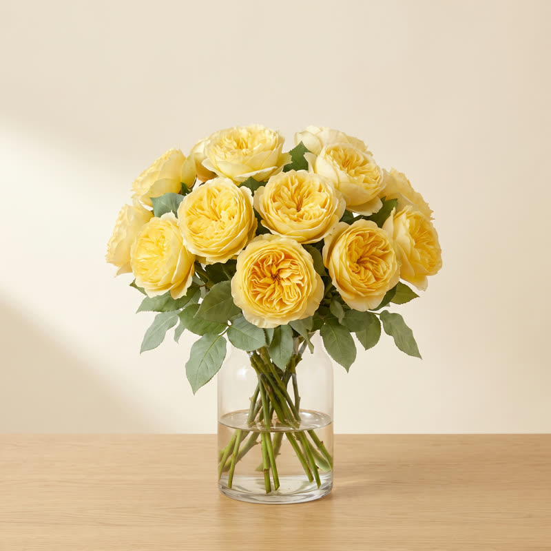 Full bouquet of ruffled yellow garden roses in a clear glass vase
