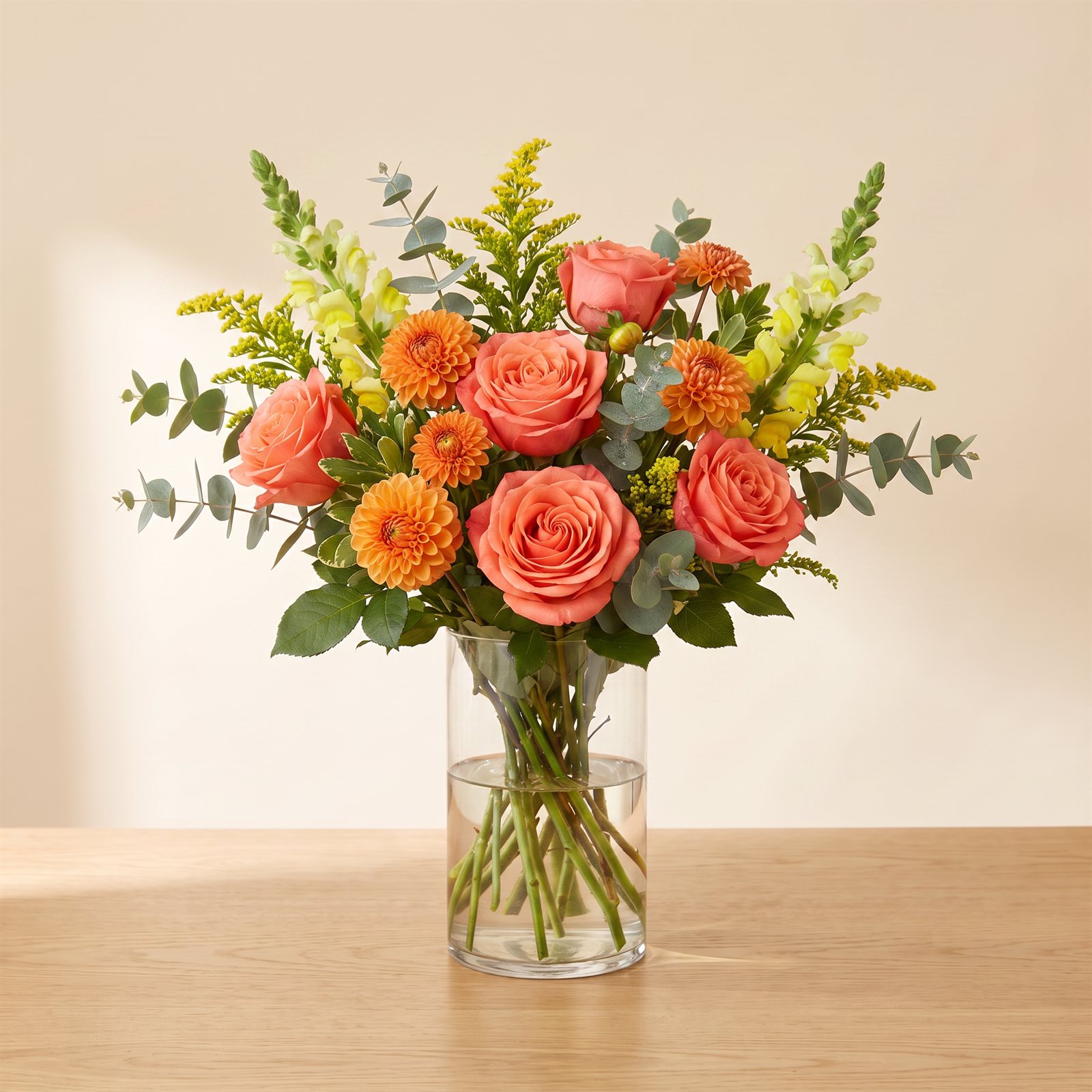 Bright designer's choice arrangement in corals and golds in a clear glass vase on an oak table