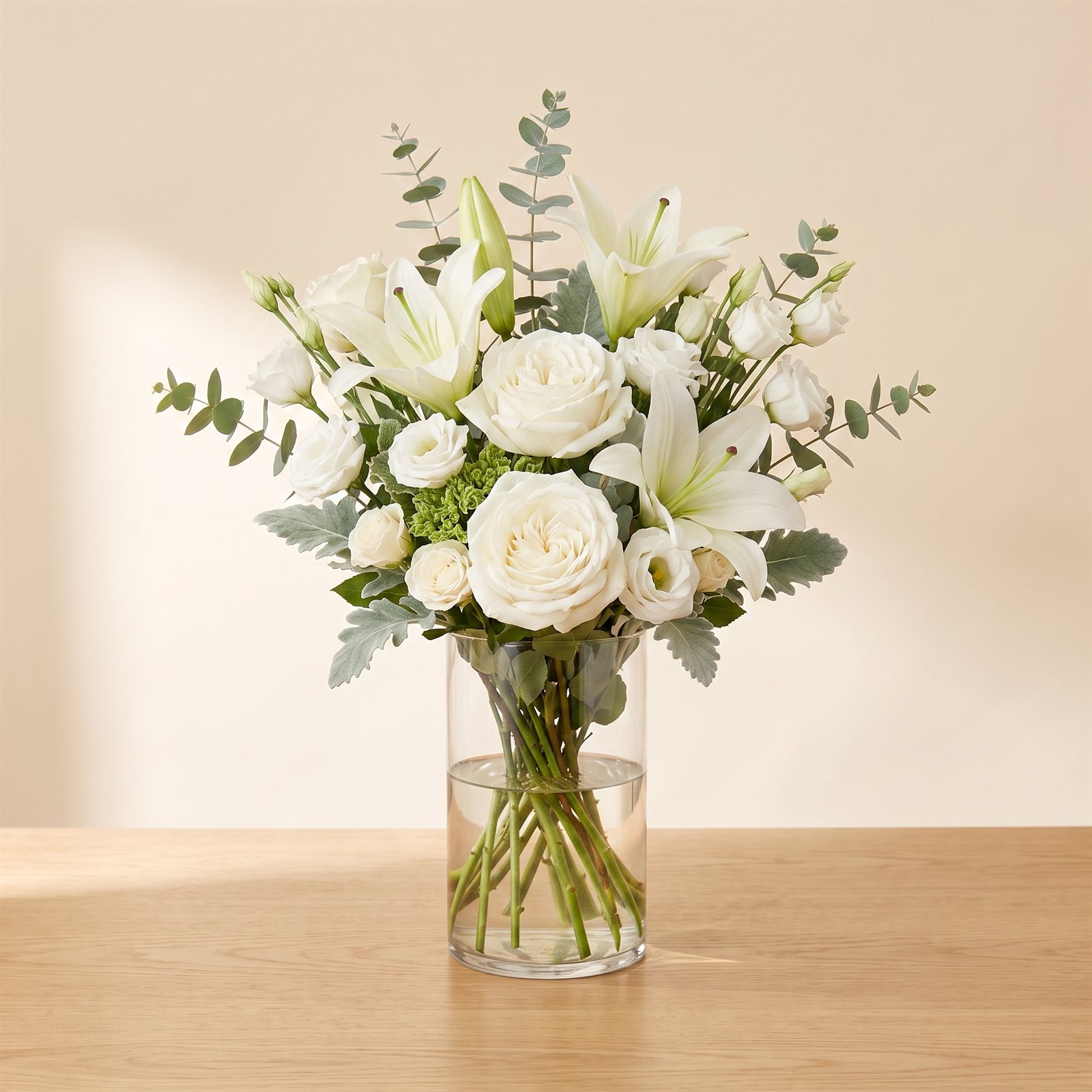 Serene all-white sympathy arrangement of roses, lilies and stock